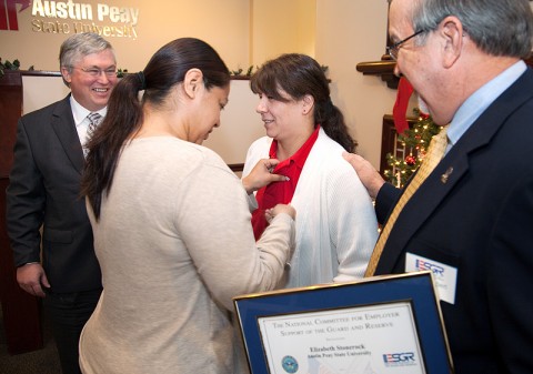 Jasmin Linares (left) places a lapel pin on Elizabeth Stonerock, recipient of the Patriot Award, presented by the Employer Support of the Guard and Reserve, during a presentation Dec. 19th at Austin Peay State University. APSU President Tim Hall (left) and retired Chief Warrant Officer 4 Carl E. Lambert, chair of ESGR’s Tennessee division, watch. (Photo by Beth Liggett, University photographer)