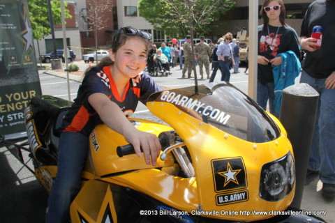 A young lady gets to sit on the Go Army Bike in the USAA Military Appreciation area