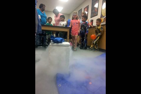 Kids get ready to hurl liquid nitrogen-frozen roses, onions and lettuce into the floor. The flowers and produce shattered like porcelain. Chilled gas escapes from the liquid nitrogen-filled cooler in the foreground. (APSU)