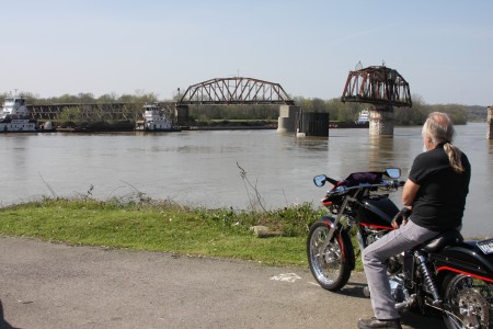 A motorcyclist watches as three Ingram Barge Company boats work to pass barges through the RJ Corman railroad bridge before the boat passes through the open bridge span and continues on up river.