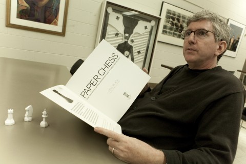 Kell Black, APSU professor of art, looks over a copy of his new book, “Paper Chess.” In front of him are a few chess pieces he designed for the book. (Photo By Rollow Welch/APSU Public Relations and Marketing)