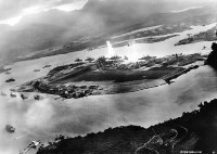 A photograph taken from a Japanese aircraft of the attack on Pearl Harbor. The photo shows Battleship Row as a torpedo impacts the USS West Virginia