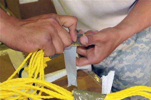 U.S. Army Staff Sgt. Carlos Gomez, wraps tape around parachute cords to keep them from getting tangled. The parachutes are attached to a pallet of supplies that will be dropped from an aircraft to ground troops at a remote forward operating base. (Photo by U.S. Army Sgt. Brent C. Powell, 3rd Brigade, 101st Airborne Division)