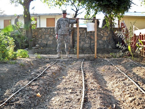 U.S. Army Staff Sgt. Robert Pharris, a ruminant specialist with the Khogyani District Agricultural Development Team attached to Company D, 1st Battalion, 138th Infantry Regiment from Mansfield, MO, stands beside a drip irrigation system the ADT constructed on Forward Operating Base Finley Shields. The system supplies water directly to the roots of plants, thereby conserving water and maximizing growth. (Courtesy photo)