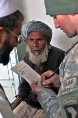 During a free clinic for local nationals, Gul Alam (center), waits on a medical assessment from Dr. Mohammed Deen (left), the director of the clinic, and U.S. Army Sgt. Robert A. Serrano, at the Mannakhil Comprehensive Health Care Center Dec. 26th. (Photo by U.S. Army Staff Sgt. Mark Burrell, Task Force Bastogne Public Affairs)