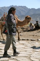 An Afghan Uniformed Police Officer walks past a camel being led by a local farmer in Naka District, Afghanistan during