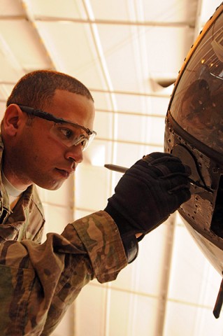 Spc. Miguel Peralta, the daytime production control representative for the airframe shop, Company B, 563rd Aviation Support Battalion touches the paint up on an OH-58 Kiowa helicopter. (Photo by Shanika Futrell)