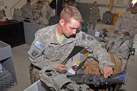 Spc. Levi White, a customs agent for the 45th Military Police Detachment, 101st Special Troops Battalion, 101st Sustainment Brigade, checks the weapon and baggage of a soldier heading home from deployment. (Photo by Sgt. 1st Class Peter Mayes)