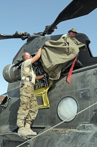 Sgt. Joshua Ommert (top), a flight engineer and Staff Sgt. Rick Carter (bottom), a flight engineer, both with Company B, 2nd Battalion, 135th Aviation Regiment, cover up an engine on a CH-47 Chinook to keep dust out while the aircraft is not in use. (Photo by Sgt. Shanika Futrell)