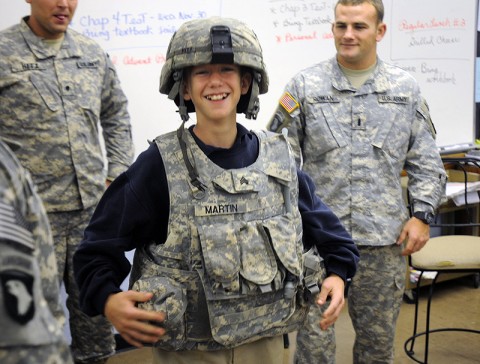 Jonah Gelhaust, a 6th grader at Saint Edwards School here, laughs while trying on the body armor and helmet of one of the soldiers from 2nd Battalion, 320th Field Artillery, 1st Brigade Combat Team Nov. 29th. The soldiers visited the school in order to build a relationship with it and the kids. (Photo by Sgt. Jon Heinrich)