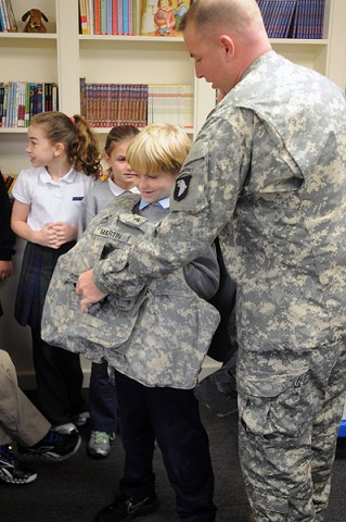 Sgt. James Martin, a chemical sergeant with 2nd Battalion, 320th Field Artillery, 1st Brigade Combat Team, helps students at Saint Edwards School try out his body armor Nov. 29th so they can have an idea of what it’s like for a soldier to wear it. (Photo by Sgt. Jon Heinrich)