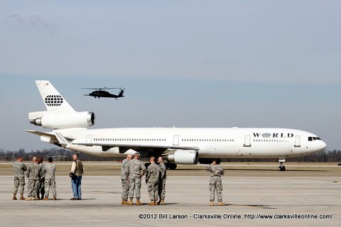 The airplane taxis for the disembarkation point while a helicopter flies down the flight line