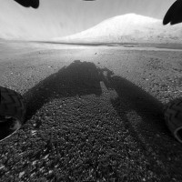 This image taken by NASA’s Curiosity shows what lies ahead for the rover — its main science target, Mount Sharp. The rover’s shadow can be seen in the foreground, and the dark bands beyond are dunes. Rising up in the distance is the highest peak Mount Sharp at a height of about 3.4 miles, taller than Mt. Whitney in California. The Curiosity team hopes to drive the rover to the mountain to investigate its lower layers, which scientists think hold clues to past environmental change. (Image credit: NASA/JPL-Caltech)