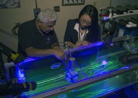 Dr. Rabi Mehta and Christina Ngo view a test of a of a traditional 32-panel football scale-model in the 17-inch water channel. Flow patterns are visualized using florescent dye and black lights. (NASA’s Ames Research Center)