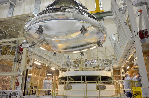 The Orion crew module for Exploration Flight Test-1 is shown in the Final Assembly and System Testing (FAST) Cell, positioned over the service module just prior to mating the two sections together. The FAST cell is where the integrated crew and service modules are put through their final system tests prior to rolling out of the Operations and Checkout Building at NASA's Kennedy Space Center in Florida for integration with its rocket. (NASA/Rad Sinyak)