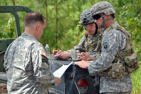 Spc. Mark E. Aescht (center), 1st Platoon, Headquarters and Headquarters Company, 160th Special Operations Aviation Regiment (Airborne) and Sgt. Derek A. Youngs (right), with 1st Platoon, HHC, 160th SOAR (A), receive instruction on writing an operations order during the Army Warrior Task lanes while competing in the United States Army Special Operations Command's Best Warrior Competition June 25, 2014. (Sgt. 1st Class Thaddius S. Dawkins II)