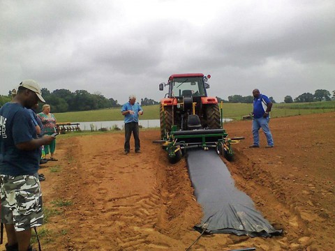 Billy & Teresa Reints McCraw demonstrating the plastic layer for plasticulture strawberries. This machine builds the beds in the soil, lays the plastic and the irrigation line all at the same time at McCraw's Strawberry Ranch.