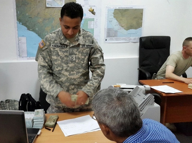 Pfc. Khatiwada Khatiwada from the 106th Financial Management Support Unit pays a local vendor in order to fund upcoming construction projects that will take place in support of Operation United Assistance. The 106th FMSU spearheaded a commercial vendor service support capability to prepare, audit and process all vouchers for supplies, services and equipment, procured by the U.S. Army in contingency operations in Europe and Africa. (Capt. Andres Leon/U.S. Army)