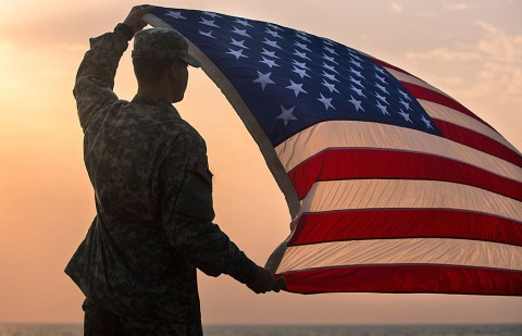 Spc. Morgan Austin, communications specialist with Joint Forces Command – United Assistance, assigned to Headquarters and Headquarters Battalion, 101st Airborne Division (Air Assault), holds up the U.S. flag during a promotion and re-enlistment ceremony Jan. 1, 2015, at Barclay Training Center, Monrovia, Liberia. (Spc. Rashene Mincy, 55th Signal Company (Combat Camera))