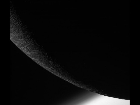 NASA's Cassini spacecraft paused during its final close flyby of Enceladus to focus on the icy moon's craggy, dimly lit limb, with the planet Saturn beyond. (NASA)