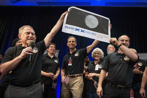 Pluto Explored. (left to right): New Horizons Principal Investigator Alan Stern of Southwest Research Institute (SwRI), Boulder, Colorado; New Horizons’ Deputy Project Scientist Leslie Young, SwRI; Johns Hopkins University Applied Physics Laboratory (APL) Director Ralph Semmel; Annette Tombaugh, daughter of Clyde Tombaugh, who discovered Pluto in 1930; and New Horizons Co-Investigator Will Grundy, Lowell Observatory, Flagstaff, Arizona hold a print of the 1991 Pluto stamp –with their suggested update – on July 14 at APL in Laurel, Maryland. (NASA/Bill Ingalls)