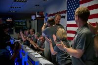 The Juno team celebrates at NASA’s Jet Propulsion Laboratory in Pasadena, California, after receiving data indicating that NASA’s Juno mission entered orbit around Jupiter. Rick Nybakken, Juno project manager at JPL, is seen at the center hugging JPL’s acting director for solar system exploration, Richard Cook. (NASA/JPL-Caltech)