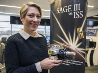 Brooke Thornton, of NASA’s Langley Research Center in Hampton, Virginia, is the mission operations manager for SAGE III on the International Space Station. She is holding a scaled model of the instrument. (NASA/David C. Bowman)