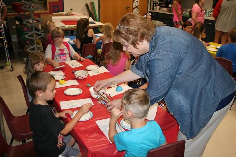 Arts for Hearts leader Rita Arancibia assists youngsters at the Public Library as they get ready to paint Kindness Rocks.