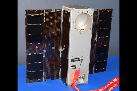 The Microwave Radiometer Technology Acceleration (MiRaTA) satellite, a 3U CubeSat, is shown with solar panels fully deployed, flanking the body of the spacecraft, which has a circular aperture at the top for the microwave radiometer antenna, used for atmospheric science measurements. There are also two small, thin tape-measure antennas on the top, used for UHF radio communication with the ground station. (MIT Lincoln Laboratory)