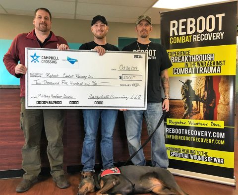 John Bredehoeft (left), presents a check to REBOOT Combat Recovery representatives Bryan Flanery and SFC (Ret) Eric Boss with his service dog Katana.