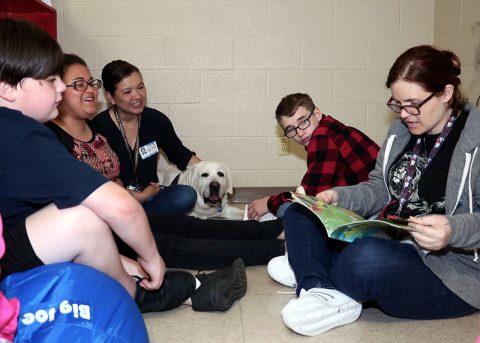 Northeast Middle School teacher Jennifer Parrish reviews reading material with students and Blanchfield Army Community Hospital pathology technician and animal assisted therapy volunteer Angela Barnett and therapy dog Samson. Barnett, Samson and other hospital volunteers visited Northeast Middle School recently in support of a Partners in Education, a program that connects organizations in the community to help support local schools. (U.S. Army photo by Maria Yager)