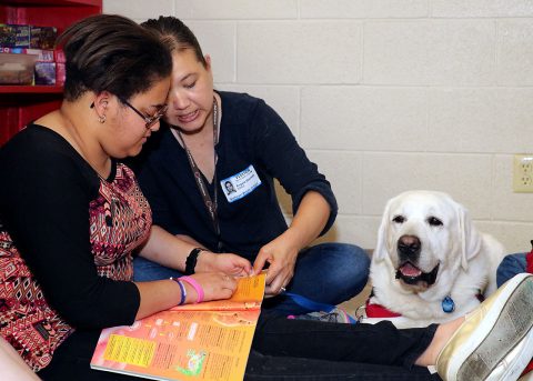 Blanchfield Army Community Hospital pathology technician and animal assisted therapy volunteer Angela Barnett and therapy dog Samson, review a book with a Northeast Middle School student during a recent Partners in Education visit to the school. Blanchfield staff regularly volunteer their time assisting teachers and students at the middle school. (U.S. Army photo by Maria Yager)