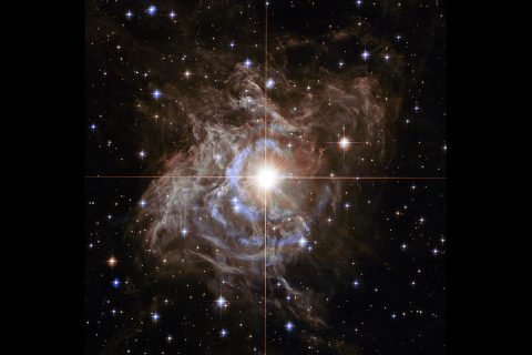 NASA Hubble Space Telescope's cosmic holiday wreath is made up of sparkling stars with RS Puppis, a type of variable star known as a Cepheid variable. As variable stars go, Cepheids have comparatively long periods — RS Puppis, for example, varies in brightness by almost a factor of five every 40 or so days. RS Puppis is unusual; this variable star is shrouded by thick, dark clouds of dust enabling a phenomenon known as a light echo to be shown with stunning clarity. These Hubble observations show the ethereal object embedded in its dusty environment, set against a dark sky filled with background galaxies. (NASA, ESA and the Hubble Heritage Team (STScI/AURA) – Hubble/Europe Collaboration; Acknowledgement: H. Bond (STScI and Pennsylvania State University)