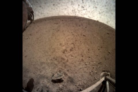 NASA's InSight spacecraft flipped open the lens cover on its Instrument Context Camera (ICC) on Nov. 30, 2018, and captured this view of Mars. Located below the deck of the InSight lander, the ICC has a fisheye view, creating a curved horizon. Some clumps of dust are still visible on the camera's lens. One of the spacecraft's footpads can be seen in the lower right corner. The seismometer's tether box is in the upper left corner. (NASA/JPL-Caltech)