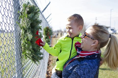 Kim Fields, Wreaths Across America volunteer, holds her 3-year-old grandson, Austin, Saturday, Dec. 15, 2018, as he straightens the velvet red bow on a wreath honoring fallen service members during a Wreaths Across America ceremony on Fort Campbell, Kentucky. More than 50 volunteers worked together to hang 101 wreaths along the fence inside T.C. Freeman Gate, Fort Campbell’s main gate, to honor fallen service members. (Mari-Alice Jasper, Fort Campbell Courier) 