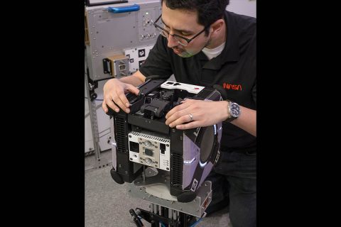 Astrobee robots are equipped with payload bays to support the installation and testing of new hardware. Jose Cortez, aerospace engineer at NASA’s Ames Research Center in Silicon Valley, checks the fit of a robot arm that locks into the top bay. The arm can be used to “perch” on one of many handrails in the International Space Station in order to conserve power while performing other operations, such as capturing video. (NASA's Ames Research Center/Dominic Hart) Astrobee robots are equipped with payload bays to support the installation and testing of new hardware. Jose Cortez, aerospace engineer at NASA’s Ames Research Center in Silicon Valley, checks the fit of a robot arm that locks into the top bay. The arm can be used to “perch” on one of many handrails in the International Space Station in order to conserve power while performing other operations, such as capturing video. (NASA's Ames Research Center/Dominic Hart)