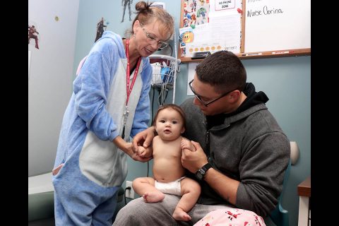 U.S. Army Staff Sgt. Michael Bottcher holds his daughter while Blanchfield Army Community Hospital nurse Pene Schrock checks the baby's vital signs during a walk-in flu vaccine clinic for beneficiaries 6 months to 17 years old, Oct. 29. Clinic staff dressed up as kid friendly characters and  administered vaccines to more than 130 children. The Centers for Disease Control and Infection recommends everyone 6 months and older get a flu vaccine every year before flu activity begins in their community. (Maria Yager)