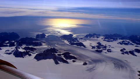 Greenland's Steenstrup Glacier, with the midmorning sun glinting off the Denmark Strait in the background. The image was taken during a NASA IceBridge airborne survey of the region in 2016. (NASA/Operation IceBridge)