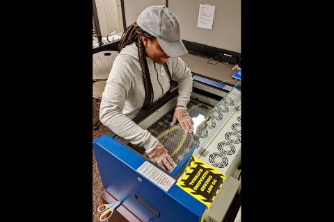 Ciara Grandberry places plastic for face shields into a laser printer. (APSU)