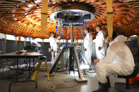 Engineers prepare for the flexible heat shield installation on the inflatable structure. The view is from bottom side, and the heat shield is on top. (NASA’s Langley Research Center) Engineers prepare for the flexible heat shield installation on the inflatable structure. The view is from bottom side, and the heat shield is on top. (NASA’s Langley Research Center)
