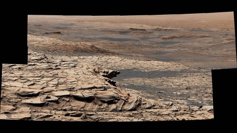 Stitched together from 28 images, NASA's Curiosity Mars rover captured this view from "Greenheugh Pediment" on April 9, 2020, the 2,729th Martian day, or sol, of the mission. In the foreground is the pediment's sandstone cap. At center is the "clay-bearing unit"; the floor of Gale Crater is in the distance. (NASA/JPL-Caltech/MSSS)