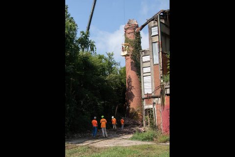 Workers inspect the structure after the top half of the smokestack came down. After a second pull by a bulldozer, the bottom half toppled, becoming a pile of dust and rubble.