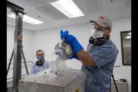 Andrew Kennett (left) watches as Dominic Aldi (right) uses liquid nitrogen to cool a motor integrated bulk metallic glass gearbox prior to shock testing it. The motor and gearbox are inside the frosty metal “bucket” that contains the liquid nitrogen. The tooling, including the “bucket” is designed to be mounted both vertically (shown) and horizontally on the cube for testing the motor and gearbox in three orientations. (NASA/JPL-Caltech)