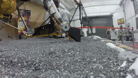 This photo from Aug. 19, 2019, shows a replica of InSight scraping soil with a scoop on the end of its robotic arm in a test lab at JPL. A replica of the "mole" - the lander's self-hammering heat probe - comes in to view as the scoop moves to the left. On Mars, InSight will scrape and tamp down soil on top of the mole to help it dig. (NASA/JPL-Caltech)