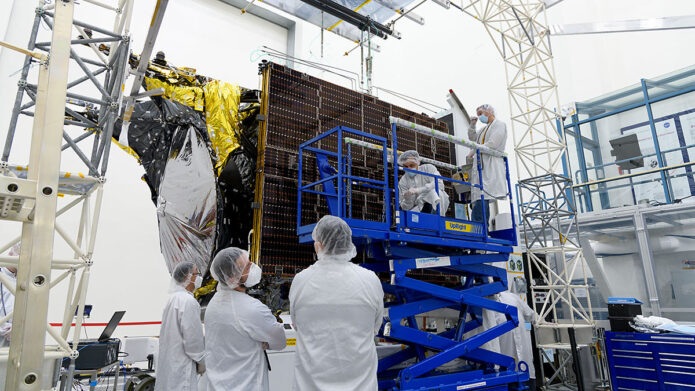 Before a deployment test in a clean room at JPL, engineers examine one of Psyche’s two solar arrays. The arrays are folded and stowed flush with the chassis, as shown here, before launch and then deployed in flight. (NASA/JPL-Caltech)