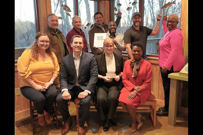 (L to R front row) Sally Burchett, Wade Bourne Nature Center Foundation Member Wes Sumner, Montgomery County Parks and Recreation Natural Resources and Program Manager Katherine Netti (holding check) and Montgomery County Trustee Kimberly Wiggins. (Back row) Montgomery County Parks and Recreation Committee Member Mike Taliento, Montgomery County Parks and Recreation Committee Member Ronnie Boyd, Mayor Golden, County Commissioner Jason Knight, County Commissioner Chris Rasnic and County Commissioner Rashidah Leverett standing in the location of the future fish tank.