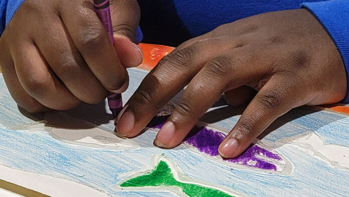 Austin Peay State University freshman education major Maliyah Green colors in one of freshman studio art major Kayla Cross’s artworks. The simple design and tactile elements allow Green, who is blind, to imagine and color the picture easily. (APSU)